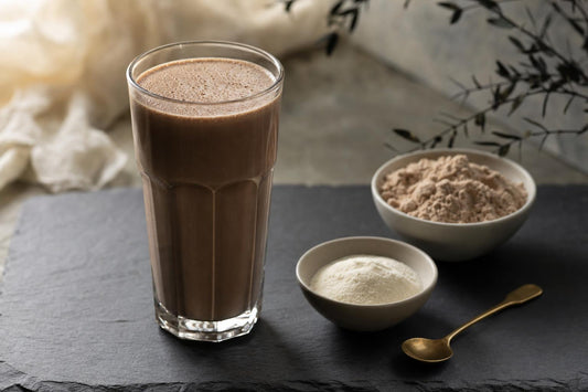 A tall glass of chocolate protein drink beside small bowls of collagen peptides and bone broth protein powder