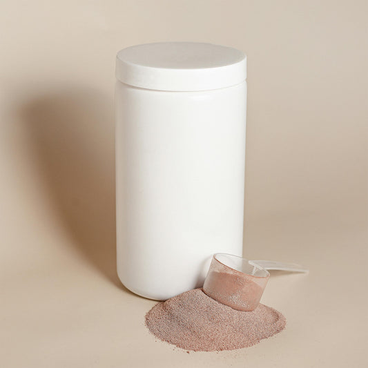 A plain white protein powder container with a scoop of powder spilled beside it on a neutral background